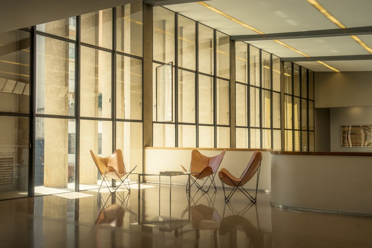 A sunlit lounge with leather chairs by a tall glass wall