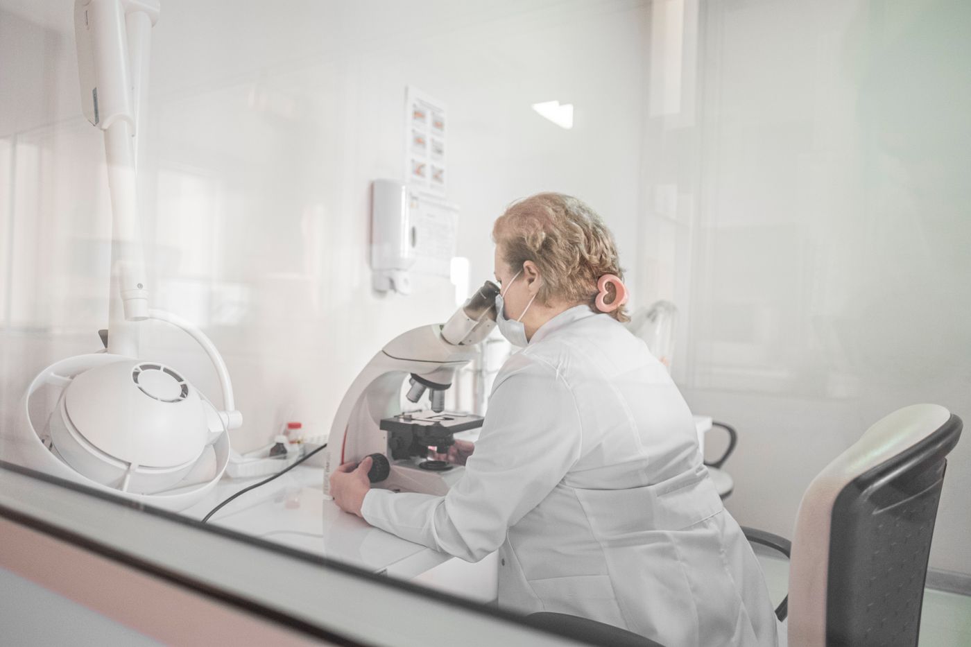 A researcher at a microscope seen through laboratory glass